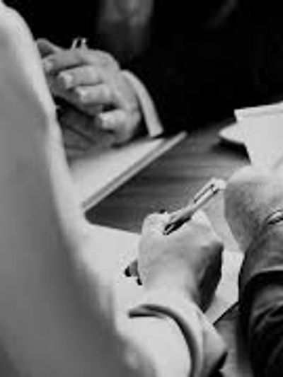 Two people in a meeting, one holding a pen and writing on paper.