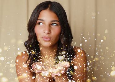 Woman blowing sparkling glitter from her hands with a soft smile.