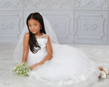 Young girl in a white dress holding a bouquet, sitting gracefully.