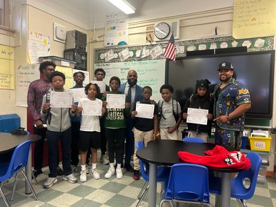 A group of students and two adults holding certificates in a classroom.