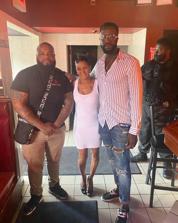 Three people posing together inside a restaurant with a security guard in the background.