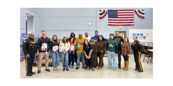 Community group posing indoors with police officers and holding bags, under an American flag.