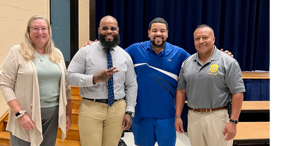 Four people smiling and posing indoors in casual and business attire.