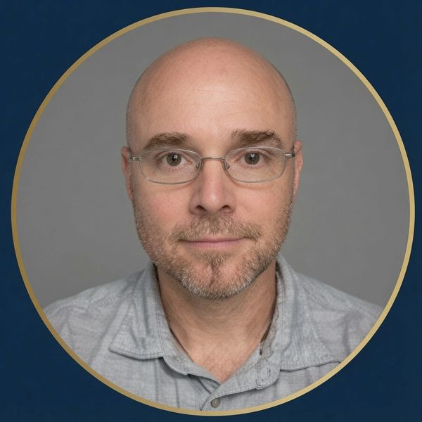 Portrait of a bald man with glasses and a light beard wearing a gray shirt.