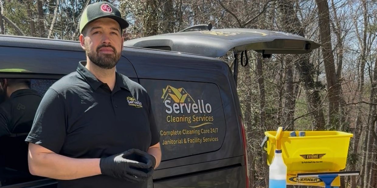 Uniformed cleaner wearing gloves standing by van next to ladder with cleaning chemicals