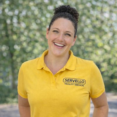 a smiling professional cleaner in uniform tidying up a common area in a commercial facility