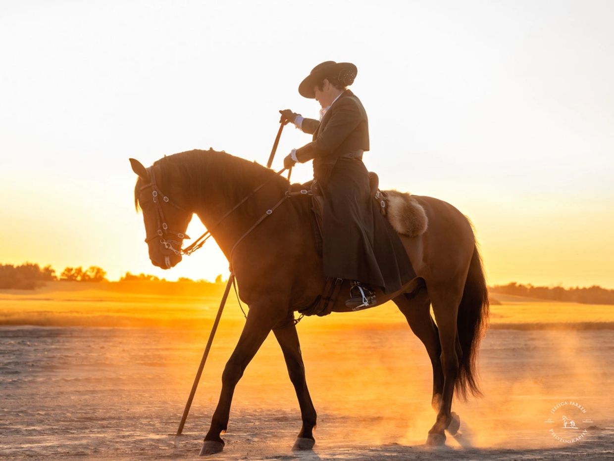 Person in traditional attire riding a horse at sunset.