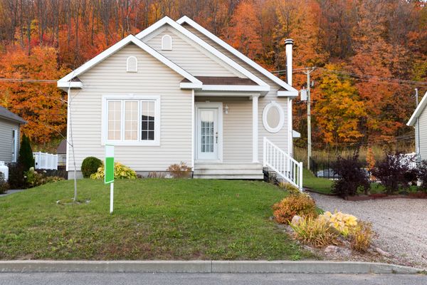 A cozy single-family home with beige siding and white trim, set against a vibrant autumn forest.