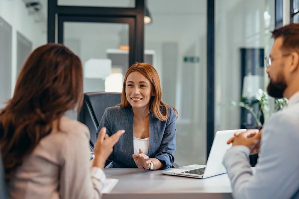 Three professionals having a conversation in an office setting.