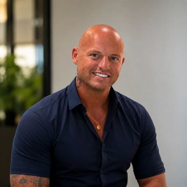 Smiling bald man in a navy shirt with tattoos.