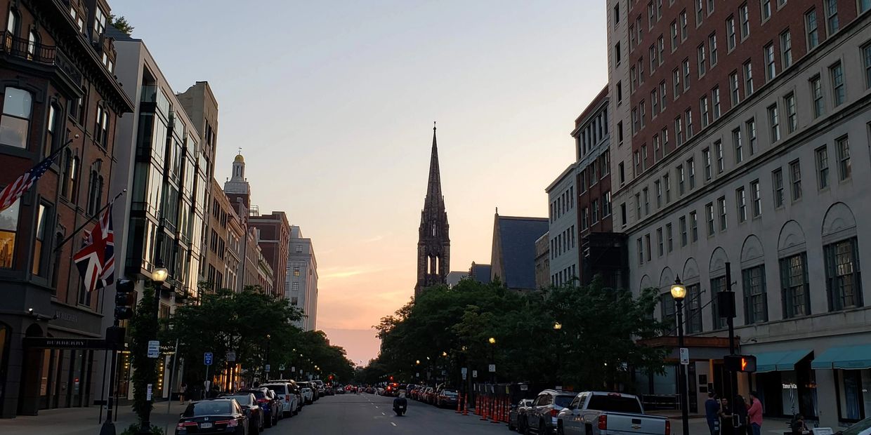 Sunset view of a city street with historic buildings and a church steeple.