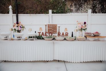 Elegant outdoor taco bar setup with flowers and toppings.