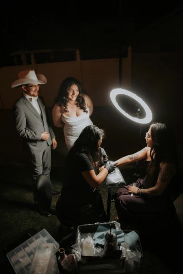 Woman getting a tattoo under a ring light while others watch.