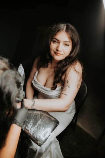 Young woman getting a tattoo on her arm in a dimly lit room.