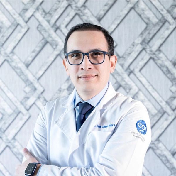 Médico con bata blanca y gafas sonriente.
