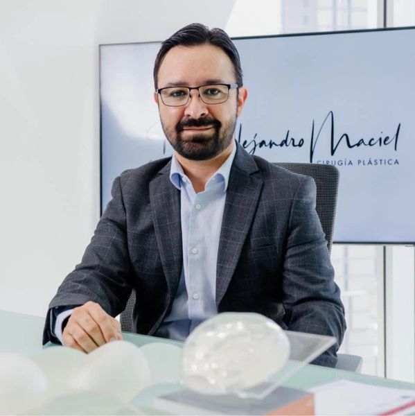 Hombre con gafas y saco sentado en escritorio.