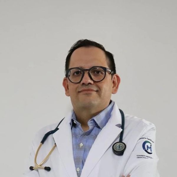 Medico internista parado de frente sonriendo a la camara portando su bata y un estetoscopio