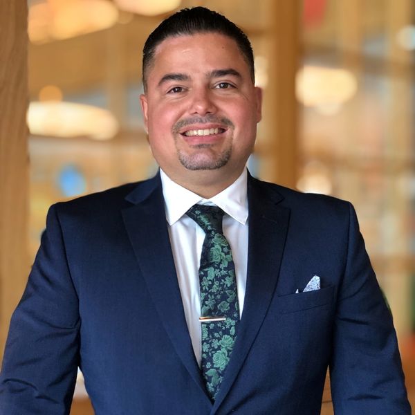 Man in a navy blue suit with a floral tie smiling.