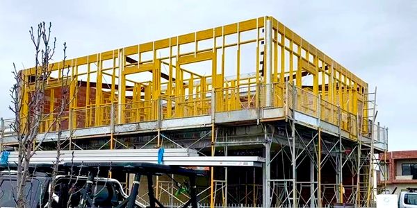 A two-story building under construction with yellow framing and scaffolding.