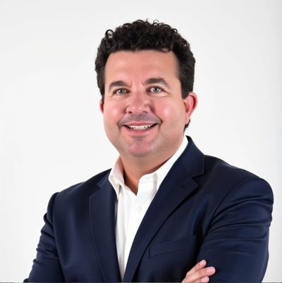 Smiling man in a navy suit with arms crossed against a plain white background.