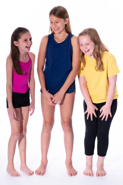 Three girls laughing together barefoot on white background.