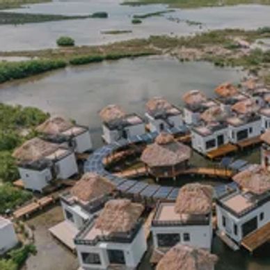 Aerial view of thatched-roof huts arranged in a circular pattern over water.