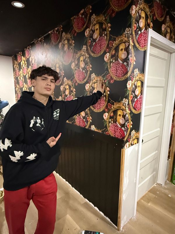 A young man poses in front of a wall with quirky bubblegum-blowing portraits wallpaper.