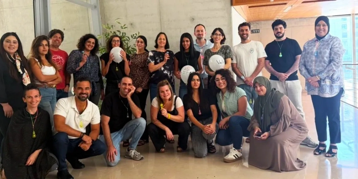 A diverse group of people posing together indoors, some holding balloons.