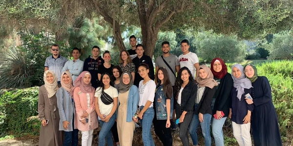 Group of young adults posing outdoors under a tree on a sunny day.