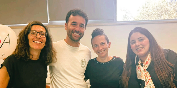Four friends smiling indoors, standing close together in casual attire.
