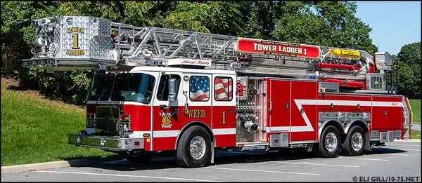 Red and white Tower Ladder 1 fire truck parked in a lot on a sunny day.