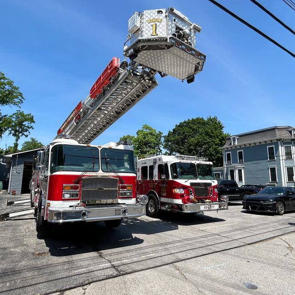 Two fire trucks parked on a street with an extended ladder under a clear blue sky.