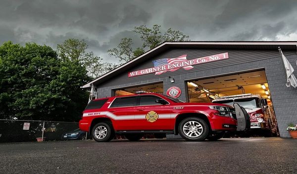 Red fire chief SUV parked outside fire station under cloudy sky.