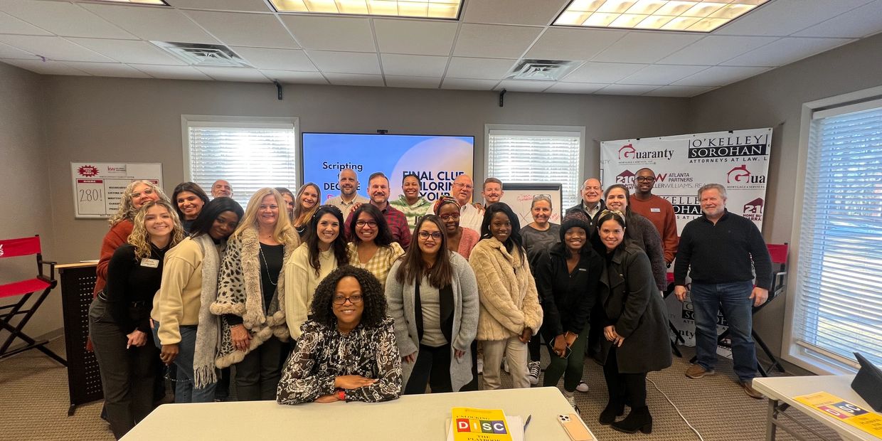 A large group of diverse people smiling in a well-lit classroom setting.