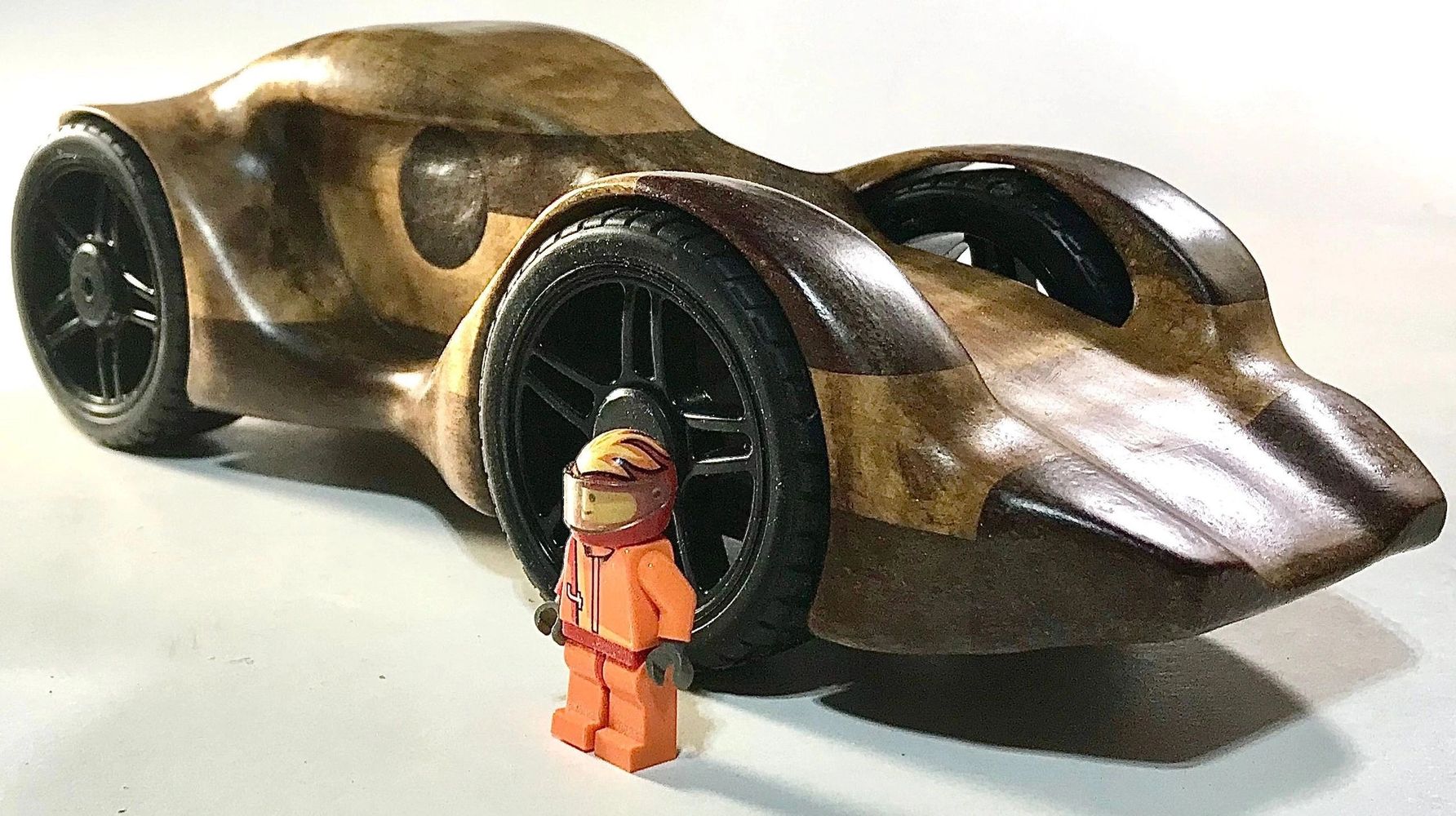 Wooden toy car with a LEGO racer figure beside it.