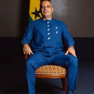 Man in a blue traditional outfit sitting on a wooden chair.