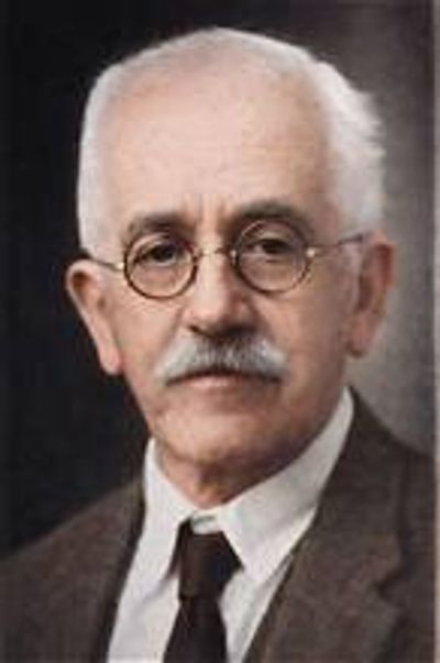 An elderly man with glasses and a mustache in formal attire.