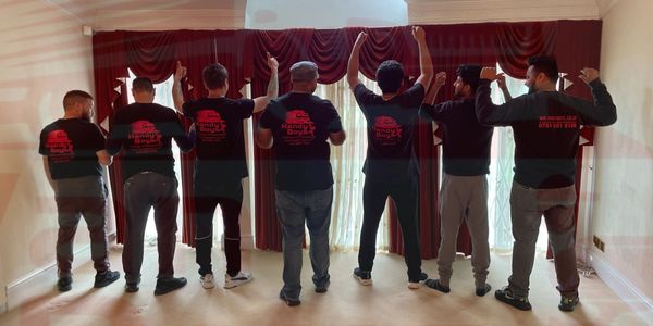 Seven men wearing matching handyman company shirts stand with backs facing the camera.