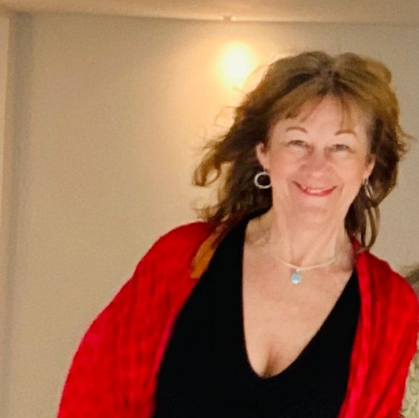 Woman smiling and dancing indoors wearing a red shawl and black outfit.