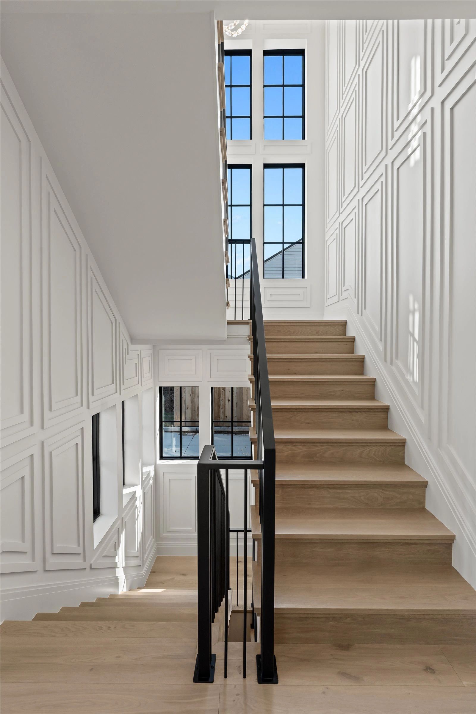 Modern staircase with wooden steps and black railing in a bright, white-walled space.