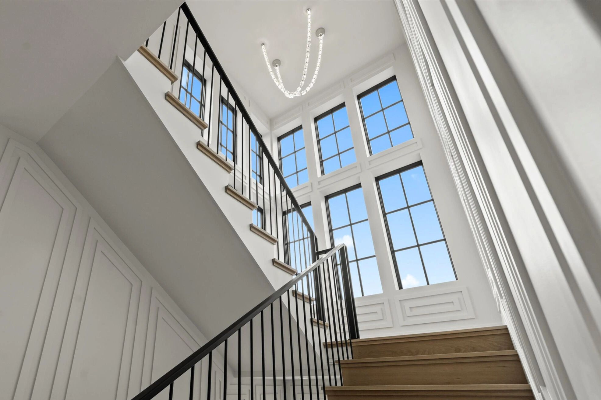 Modern staircase with black railings and large windows showing a blue sky.
