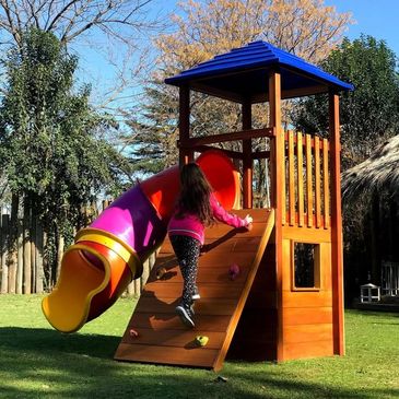 Child climbing wooden playset with colorful slide in sunny backyard.