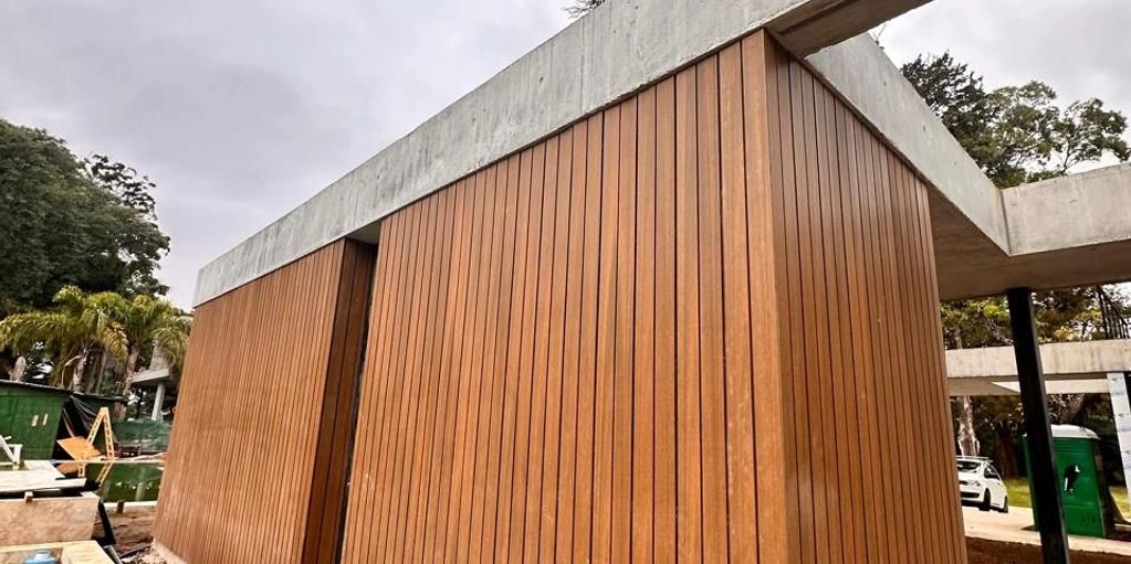 Modern building with vertical wooden panels and concrete roof under cloudy sky.