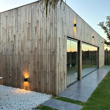 Modern wooden house with large glass doors and outdoor lighting at dusk.