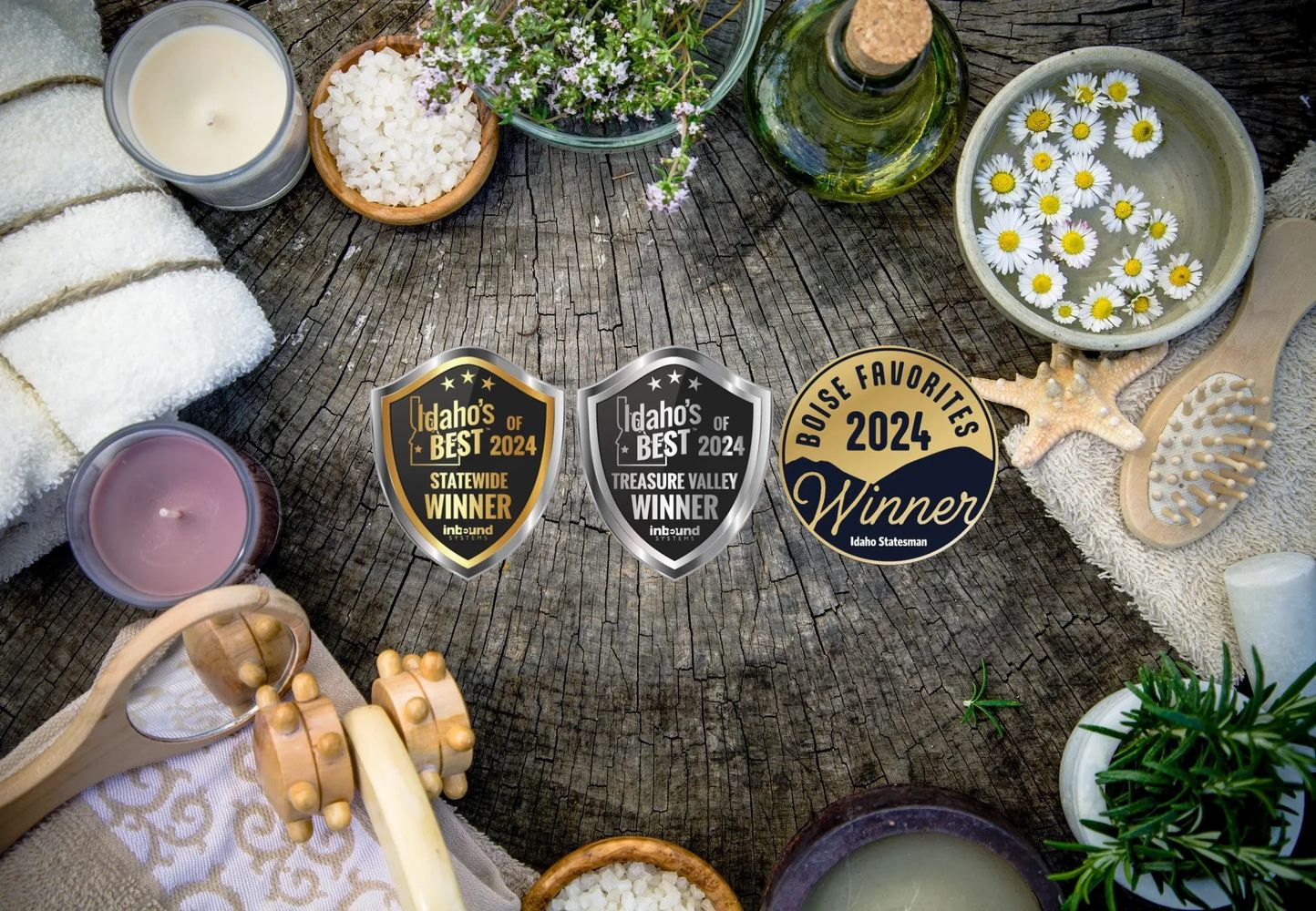 A rustic spa setup with candles, towels, flowers, and award badges on a wooden surface.