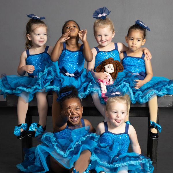 Six young girls in blue dance costumes posing playfully in a studio.