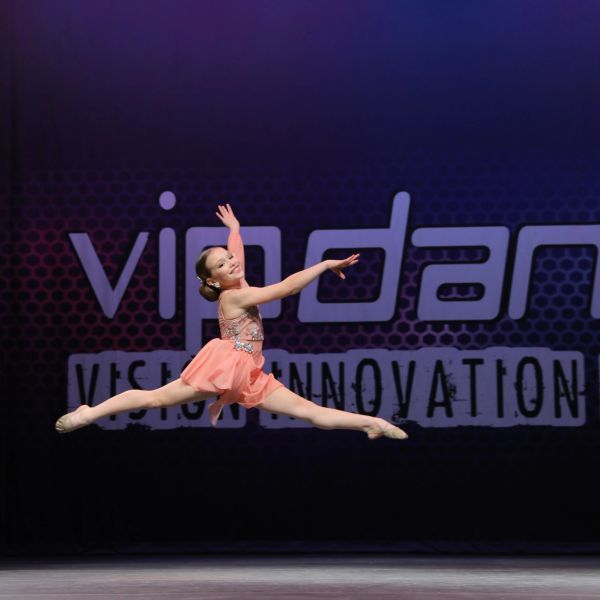 Young dancer leaps gracefully on stage in peach costume.