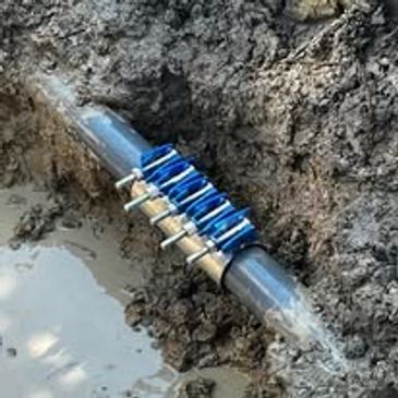 Blue clamp repairing a black pipe underground in muddy soil.
