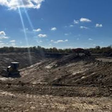 Construction vehicles working on a large dirt excavation site under a sunny sky.