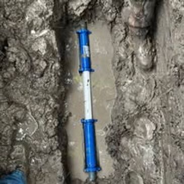 A blue and white pipe installed in a muddy trench.